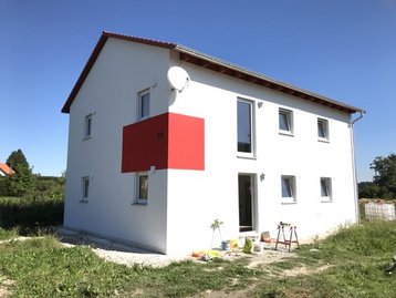 weißes Haus mit rotem Balken auf einer Wiese