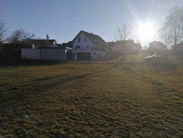 Wiese mit Haus und Sonne im Hintergrund
