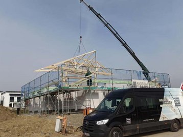 Dachstuhl an einem Kran mit Auto im Vordergrund